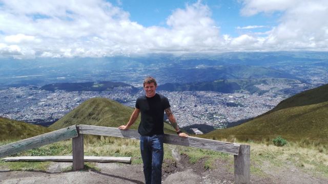 A man leaning on a wooden rail at a viewpoint high above the city of Quito.