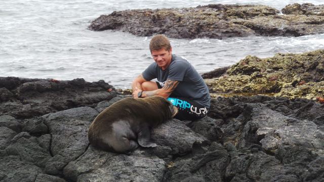 A man sitting on volcanic rocks next to a sleeping sea lion.