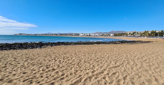 A wide sandy beach with rippled sand and calm sea under a deep blue sky.