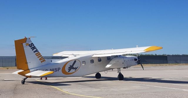A white and yellow skydiving plane parked on an airfield under a blue sky.