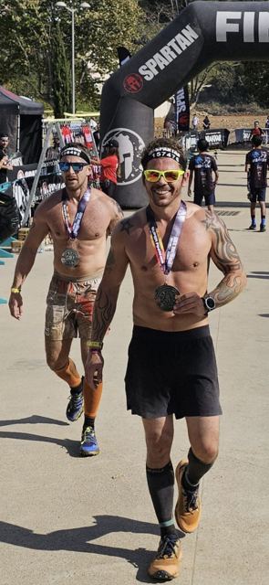 Two muddy shirtless racers walking from the finish with their medals.