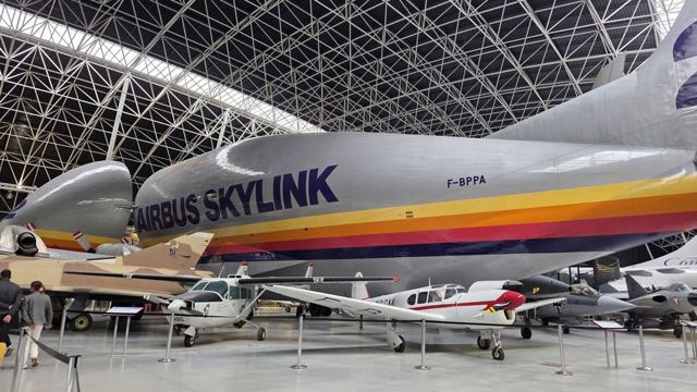 Large Airbus cargo aircraft and smaller planes displayed inside a huge hangar.