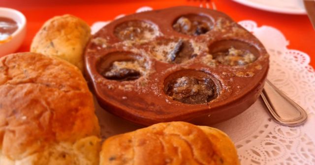 A dish of escargots in garlic butter surrounded by bread rolls on a lace doily.