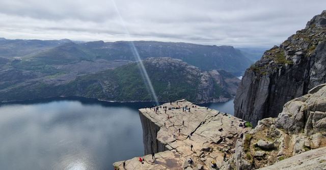 The flat-topped Pulpit Rock cliff above a fjord with a beam of sunlight cutting through cloud.