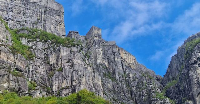 Towering grey granite cliffs with green forest below under a bright blue sky.