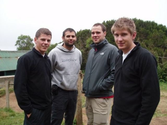 Four young men in fleeces standing together in the forest at the start of a Kilimanjaro trek.