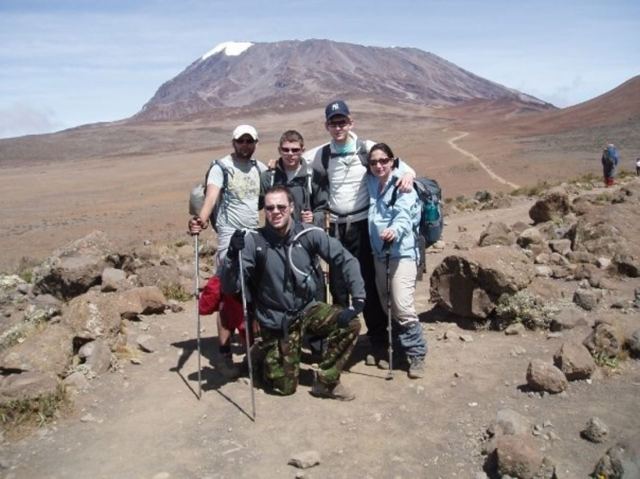 A group of trekkers posing on a rocky trail with Kilimanjaro's snow-capped Kibo summit behind them.