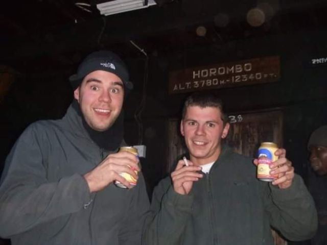 Two men in hats holding drink cans under the Horombo hut altitude sign at night.