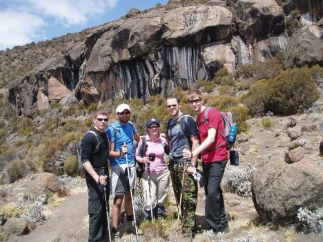 Trekkers with walking poles posing among dark volcanic rocks on Kilimanjaro.