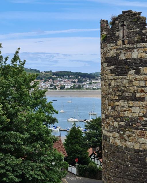 A stone tower framing a view of an estuary with moored boats and a town beyond.