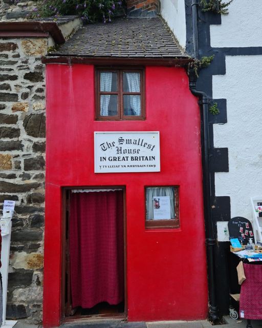 A tiny bright red house with a sign reading The Smallest House in Great Britain.