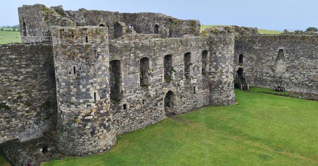 Weathered stone walls and towers of a medieval castle enclosing a green lawn.