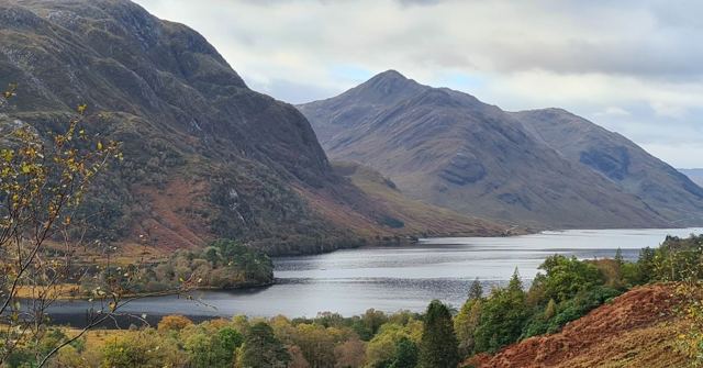 A loch surrounded by steep mountains with autumn-coloured trees in the foreground.