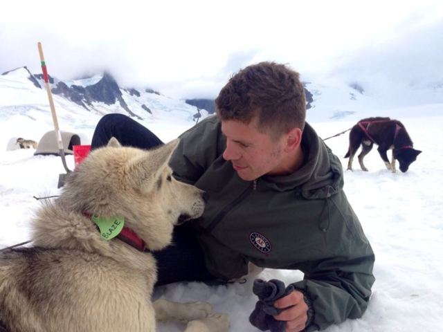 A man kneeling in the snow cuddling a husky at a dog-sledding camp on a glacier.