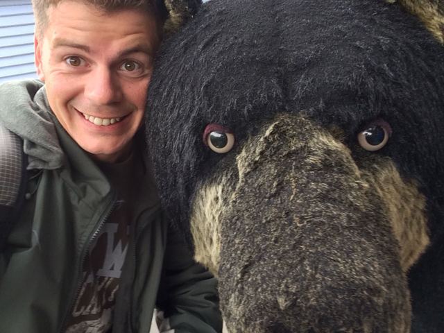 A man taking a selfie beside a large carved black bear figure.