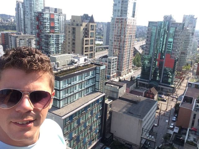 A man in sunglasses taking a selfie above the high-rise towers of Vancouver.