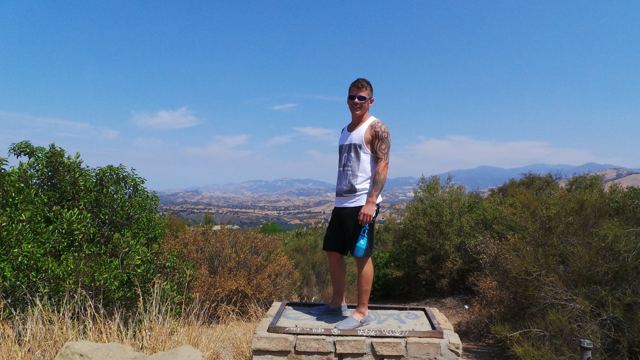 A man standing on a hilltop lookout above dry rolling hills in California.