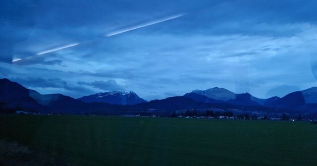 Dark blue mountains silhouetted against a dusky blue sky with an aeroplane contrail.