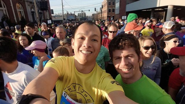 Two smiling runners taking a selfie in a crowd at the start of the Little Rock Marathon.