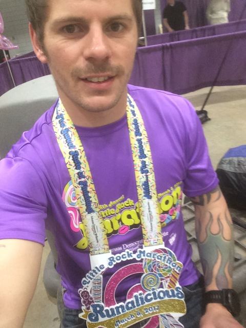 A man in a purple race top taking a selfie with an enormous marathon medal round his neck.