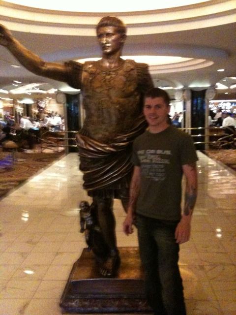A man standing next to a bronze Roman emperor statue inside a Las Vegas casino.