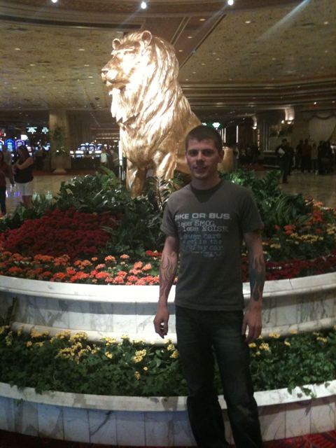 A man standing in front of a giant golden lion statue surrounded by red flowers in a casino lobby.