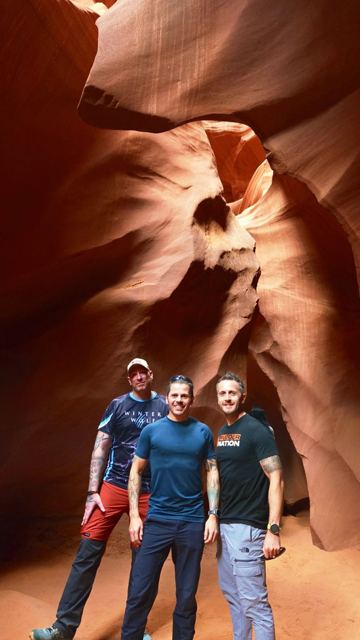 Three men standing in a narrow canyon of swirling orange sandstone walls.