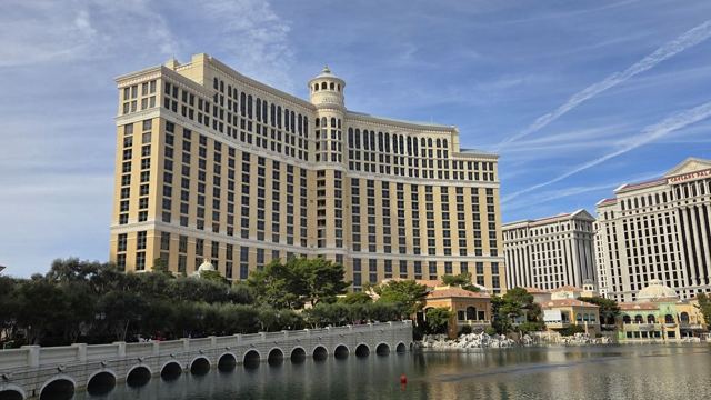 The curved Bellagio hotel tower behind its lake and balustrade under a blue sky streaked with contrails.