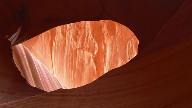 Looking up through a narrow slot canyon with smooth, glowing orange sandstone walls framing the sky.