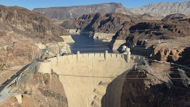 Aerial-style view of the curved concrete Hoover Dam set in a rugged rocky canyon with water behind it.