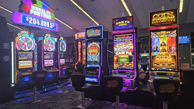 Row of brightly lit casino slot machines with a jackpot display above them.