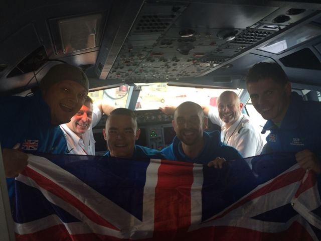 A group of men holding a Union flag on a plane, on the way to the OCR World Championships.