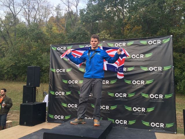 A man draped in a Union flag on a stage in front of an OCR World Championships backdrop.