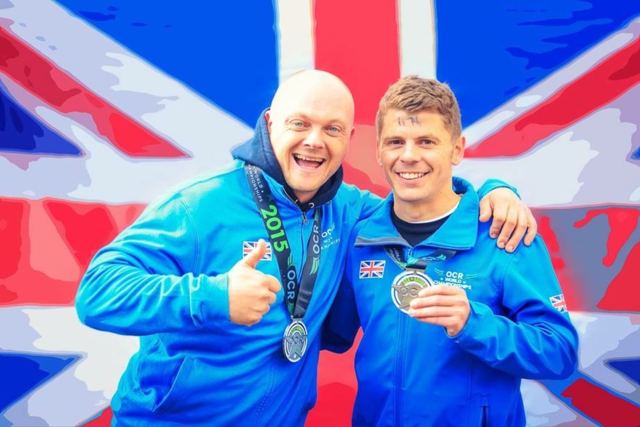 Two men in blue Team GB jackets holding medals in front of a Union flag.