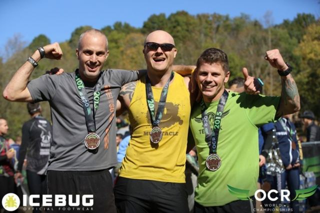 Three men in race tops flexing with their medals at the OCR World Championships finish.