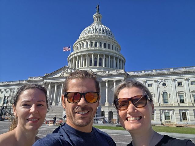 A man and two women taking a selfie in front of the US Capitol building.