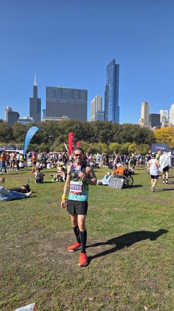 A runner in a race vest holding up his medal in Grant Park with skyscrapers behind.