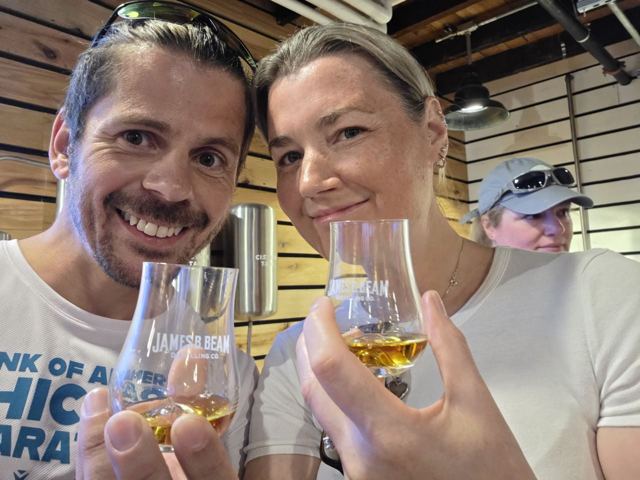 A smiling man and a woman holding small glasses of bourbon.