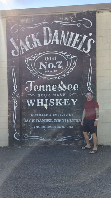 A man standing beside a giant painted Jack Daniel's Old No. 7 label on a wall.