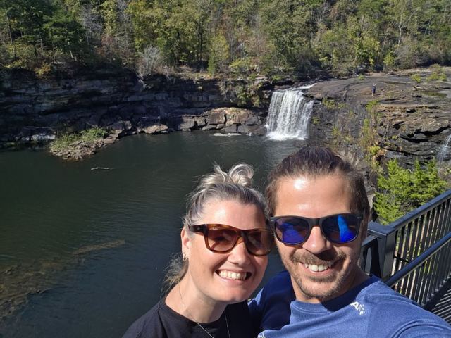 A man and a woman taking a selfie above a waterfall and river in a canyon.