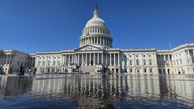 The white domed US Capitol building reflected in a shallow pool under a deep blue sky.