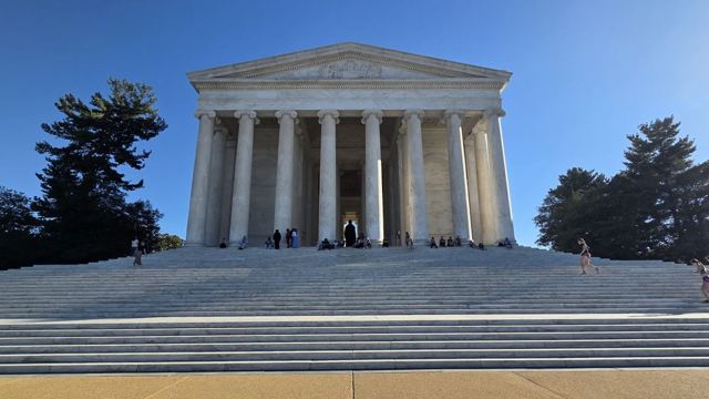 The domed, columned Jefferson Memorial at the top of wide marble steps, framed by trees.