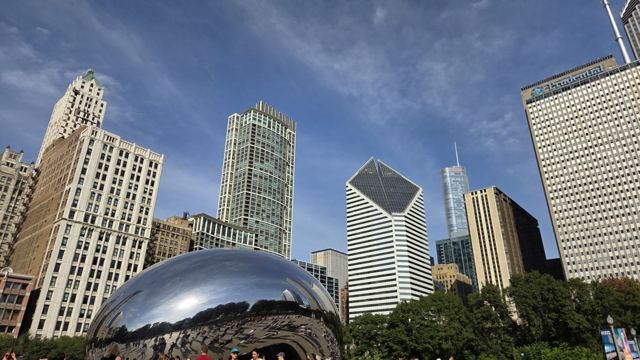The mirrored Cloud Gate sculpture reflecting surrounding Chicago skyscrapers under a blue sky.
