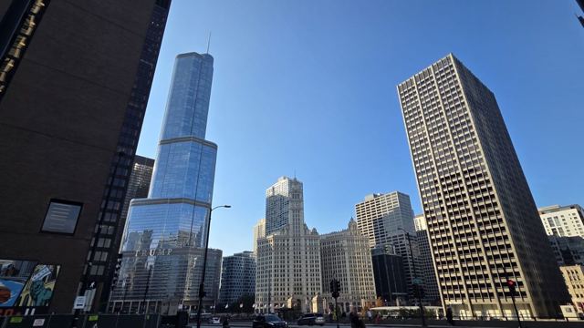 Skyscrapers, including a tall glass tower, seen from street level under a blue sky.