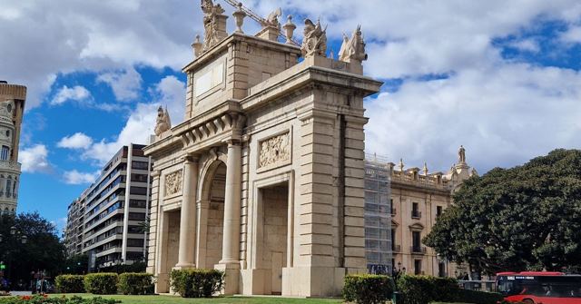 Neoclassical triumphal arch Puerta del Mar in Valencia under a blue sky with white clouds.
