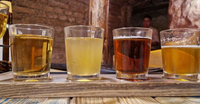 A tasting paddle of four beers of different colours on a wooden board.