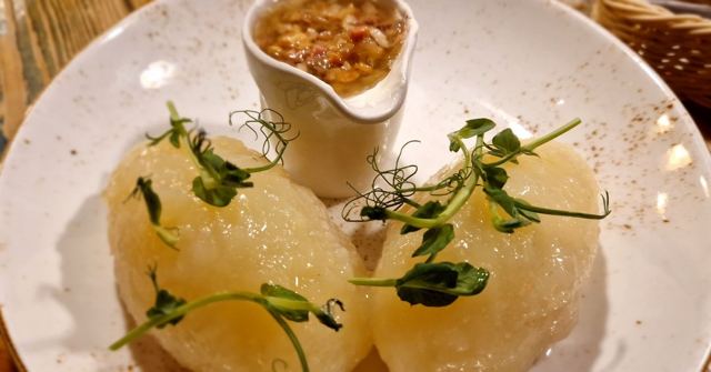 Two large potato dumplings garnished with pea shoots beside a small pot of sauce.
