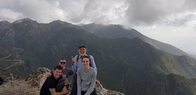 A small group of hikers on a rocky summit above green mountains in Morocco.