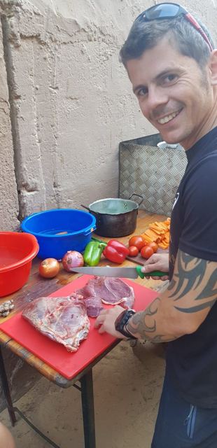 A man chopping meat and vegetables for a meal at a camp kitchen.