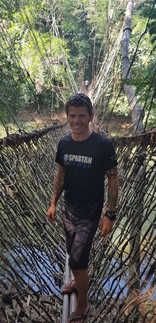 A man standing on a woven vine suspension bridge in a forest.
